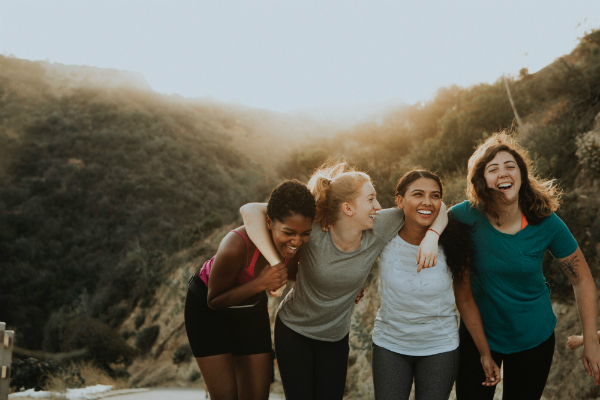 Four women sharing a group hug on a scenic mountain hiking trail