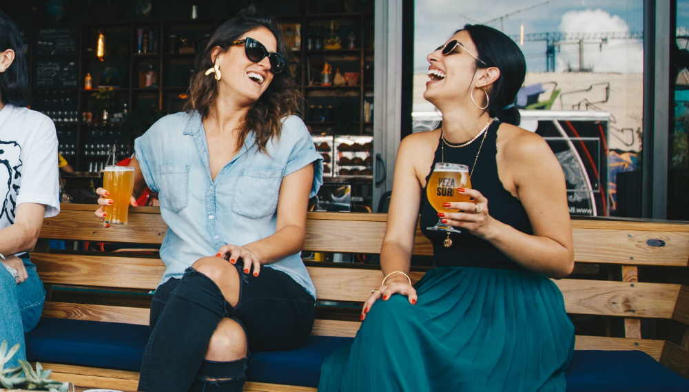 two women laughing while having a glass of beer